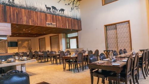 Oasis Restaurant dining area with tables and chairs arranged and a buffet counter on the side inside The Baagh Ananta Elite, Ranthambore.